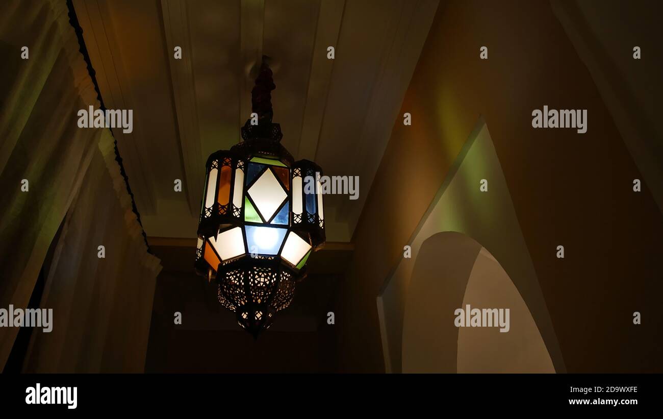 Farbenfroh verzierte Lampe im marokkanischen Stil, die den Flur eines kleinen Hotels (Riad) in der Medina von Marrakesch, Marokko bei Nacht beleuchtet. Stockfoto