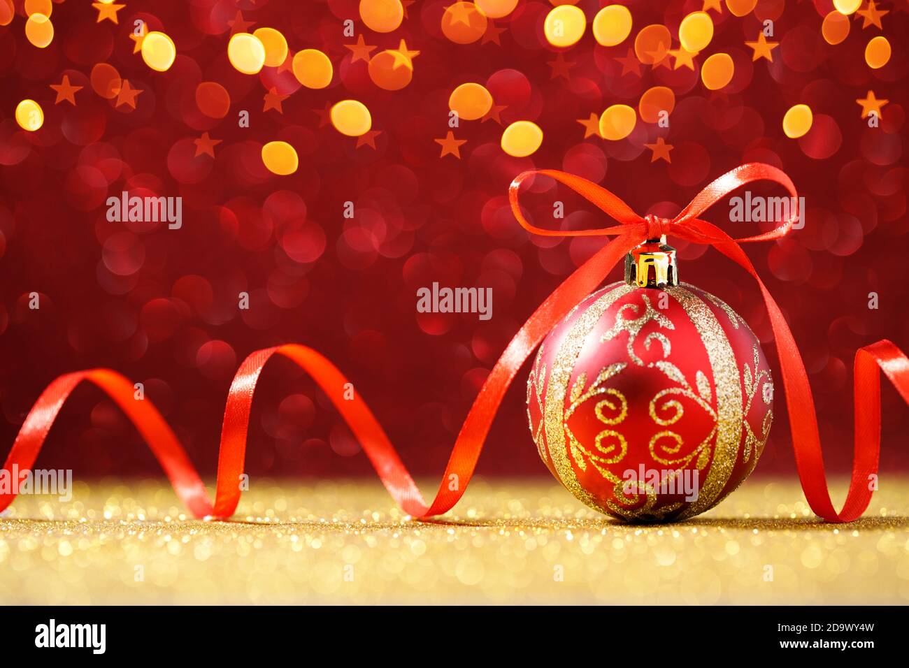 Rote Weihnachtskugel auf rotem Glitzer Hintergrund mit goldenen Lichtern Stockfoto