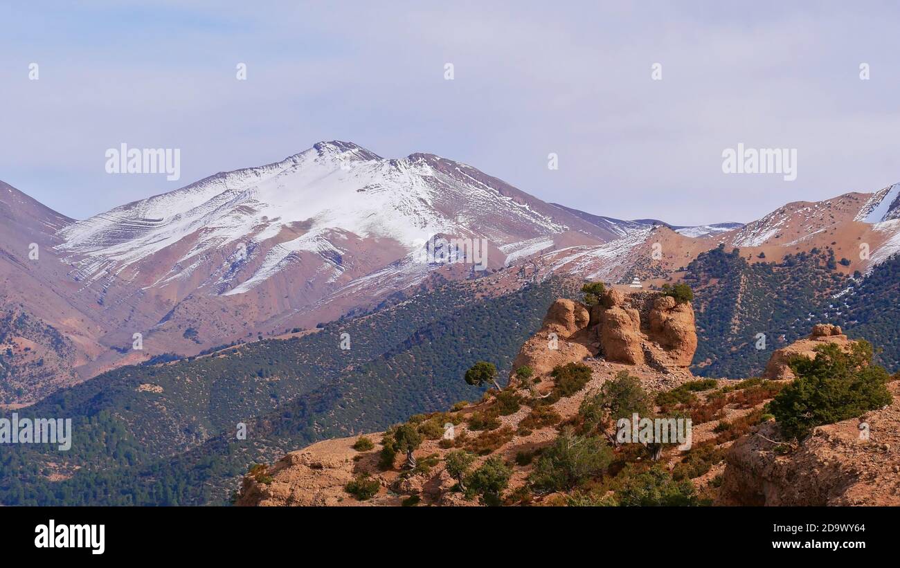 Felsformationen auf der Spitze der Kathedrale imsfrane in der Nähe von Tilouguite, Marokko, mit schneebedeckten Altas-Bergen auf einer Wanderung an einem bewölkten Wintertag. Stockfoto