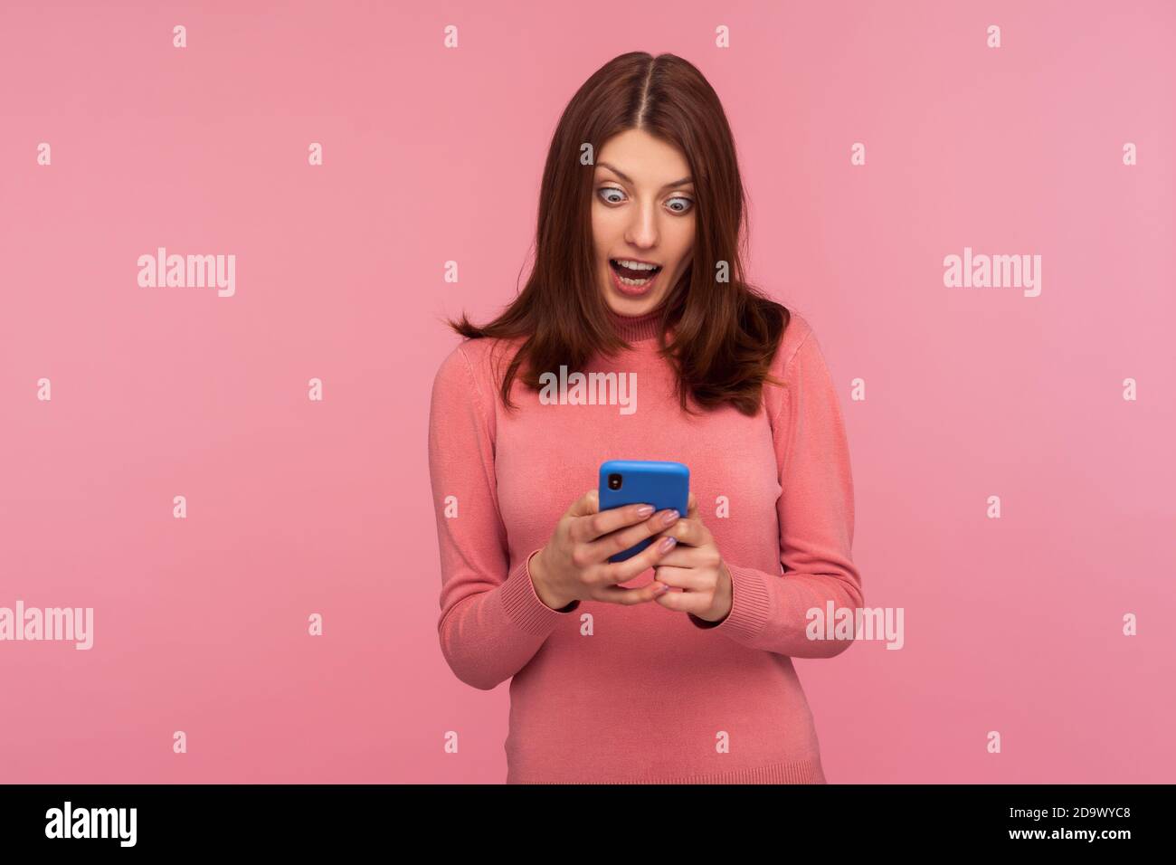 Aufgeregt Brünette Frau Blick auf Smartphone-Display in ihren Händen mit großen überrascht Augen, erhalten Nachricht über Boni und Rabatte. innenstudi Stockfoto