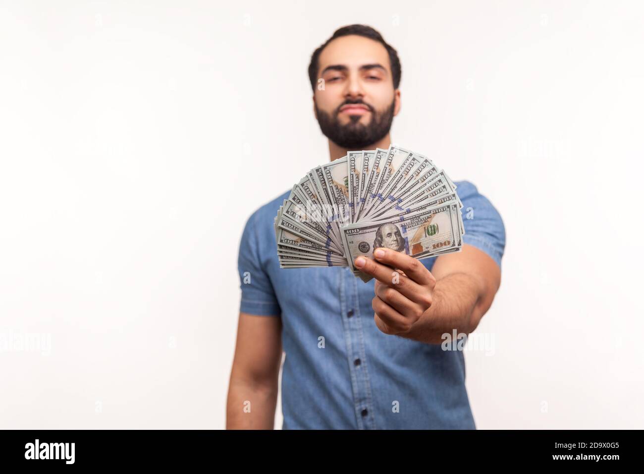 Selbstbewusster reicher Mann mit Bart in blauem Hemd, der Dollarnoten an der Kamera zeigt, mit Gehalt, Investitionen, hoher Kreditrate prahlend, Gutschrift. Indo Stockfoto