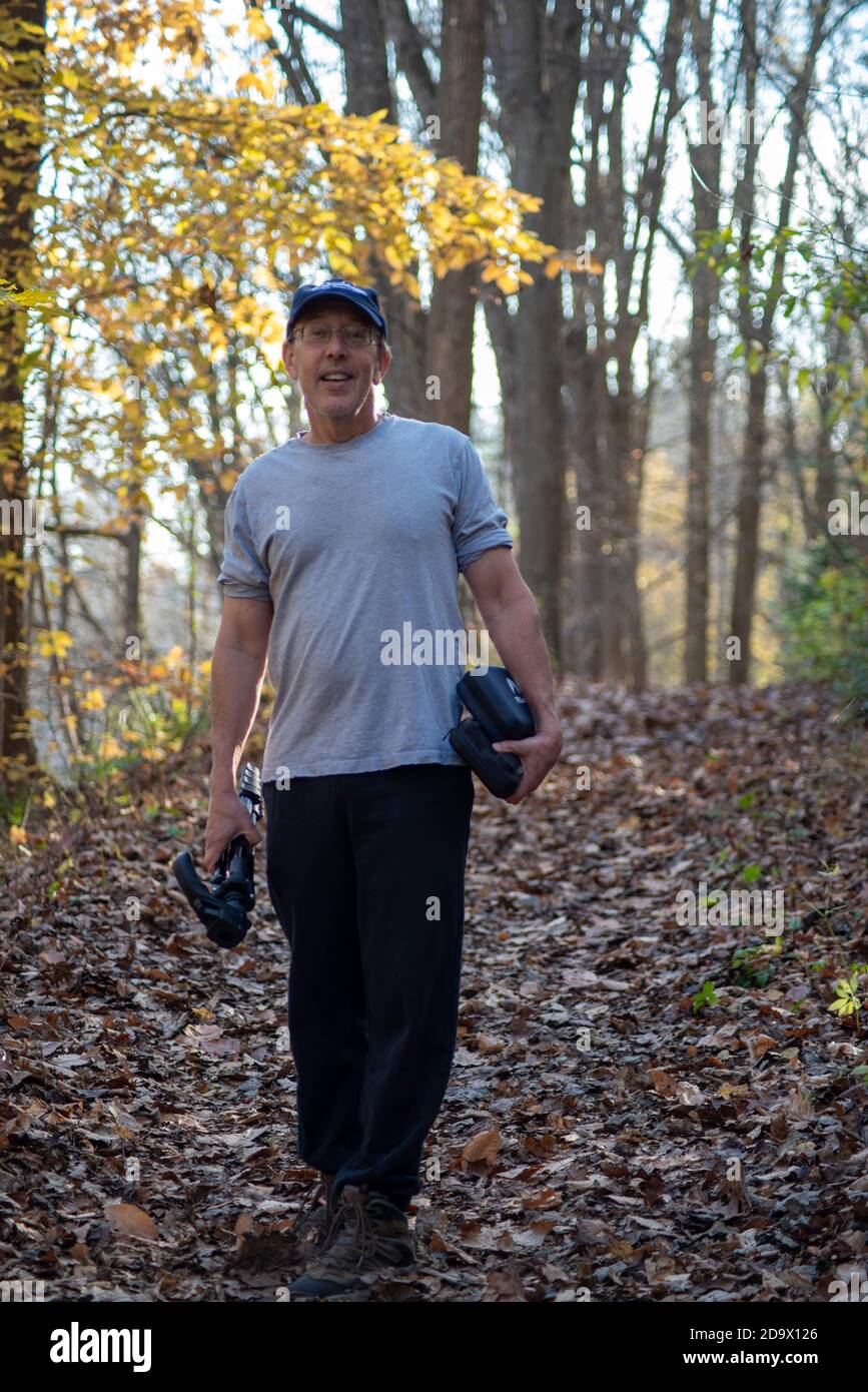 Kaukasischer Mann beim Wandern im Herbstwald mit einem Stativ Stockfoto