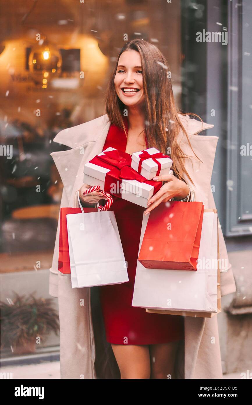 Schöne junge glückliche Frau halten Einkaufstaschen und Geschenkboxen in den Händen, lächeln im Freien. Fröhliche attraktive Mädchen Shopper haben Spaß nach Weihnachten Shop Stockfoto