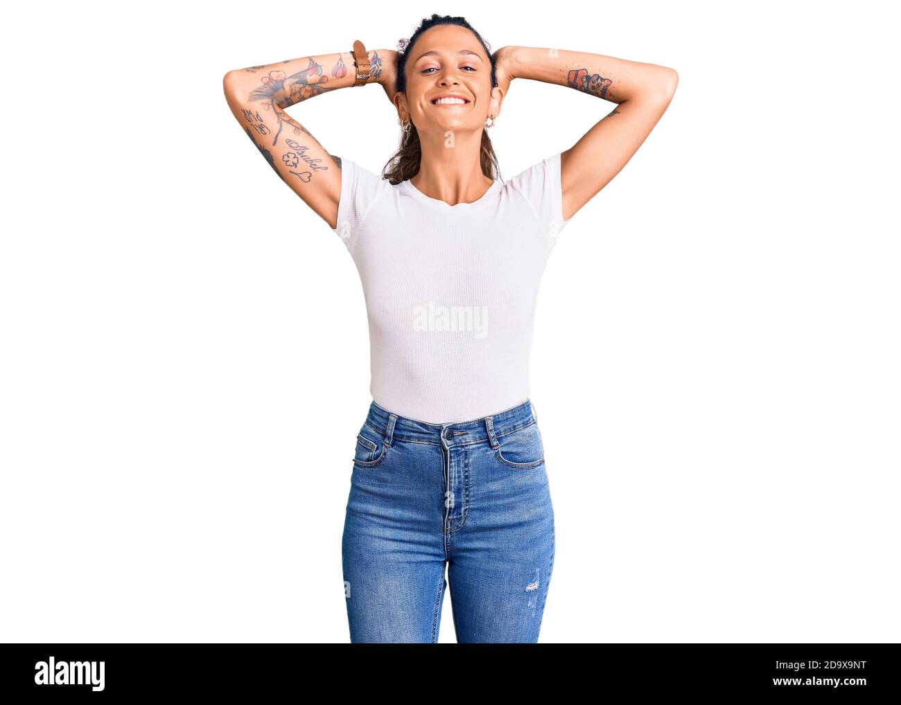Junge hispanische Frau mit Tattoo tragen lässige weiße T-Shirt entspannen und Stretching, Arme und Hände hinter Kopf und Hals lächeln glücklich Stockfoto