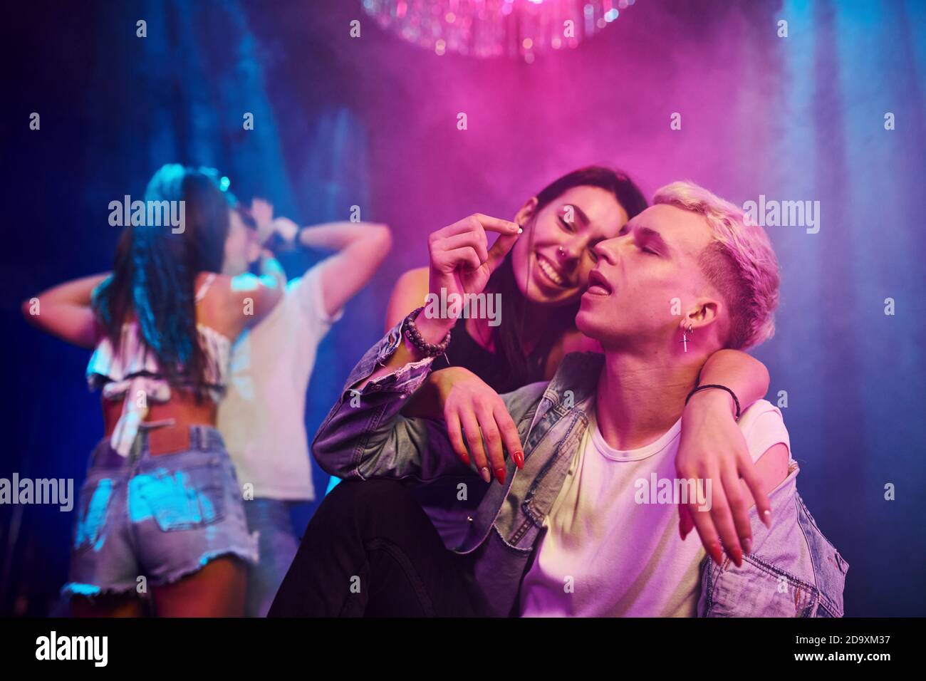 Kerl, der Drogenpille nimmt. Junge Leute haben Spaß im Nachtclub mit bunten Laserlichtern Stockfoto