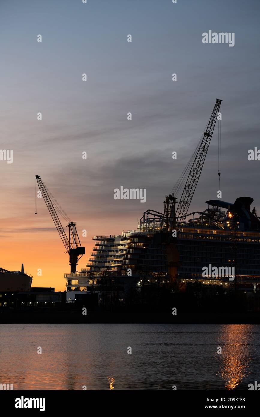 Silhouette eines Kreuzfahrtschiffes und Turmkräne in einem Schiffswerft gegen Sonnenaufgang Stockfoto