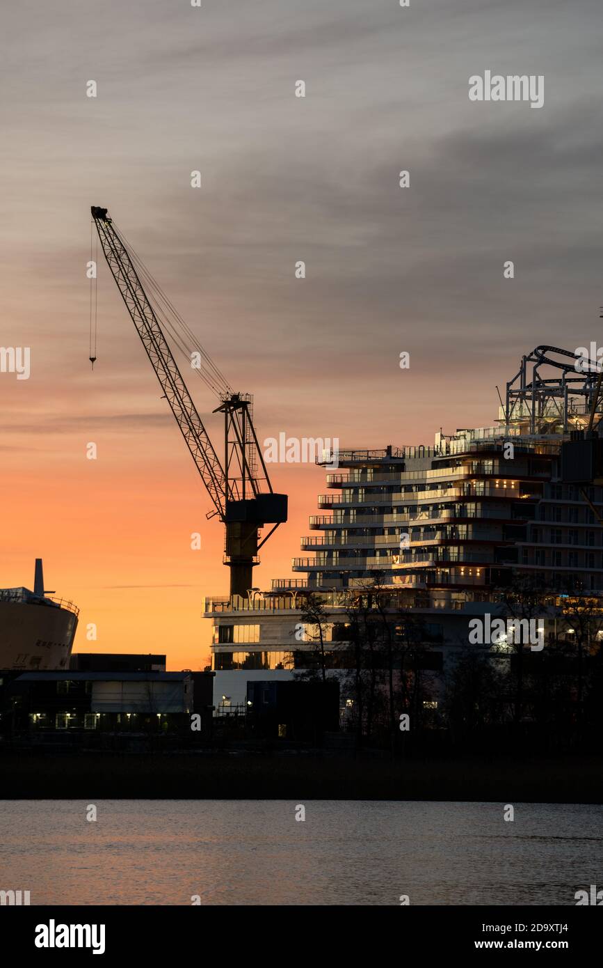 Stern eines Kreuzfahrtschiffes und eine Kransilhouette gegen bunten Himmel. Stockfoto