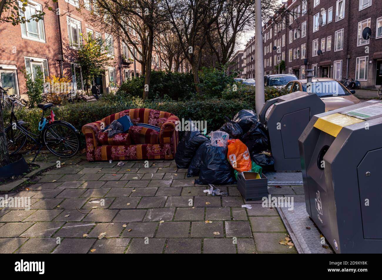 AMSTERDAM, NIEDERLANDE 21. OKTOBER 2020: Eine ausrangierte bunte Couch und ein Müllhaufen stapelten sich auf einer Straße gegen einen öffentlichen Müllcontainer Stockfoto