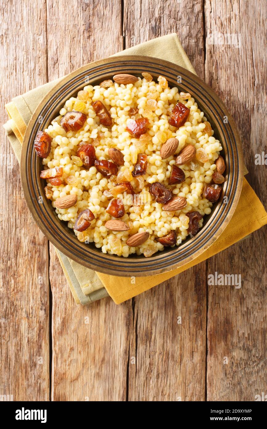 Süßer Couscous mit Mandeln, Rosinen und Datteln aus nächster Nähe auf einem Teller auf dem Tisch. Horizontale Draufsicht von oben Stockfoto