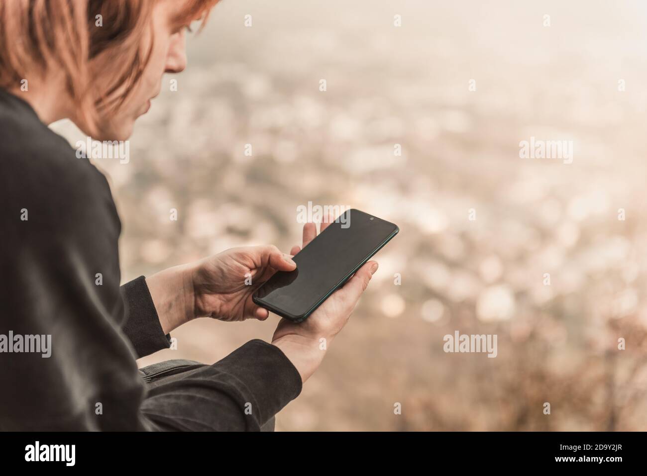 Die rothaarige Reisende Mädchen schreibt SMS auf ihr Smartphone sitzen auf dem Bergfelsen. Das Konzept von Reisen, Technologie. Stockfoto