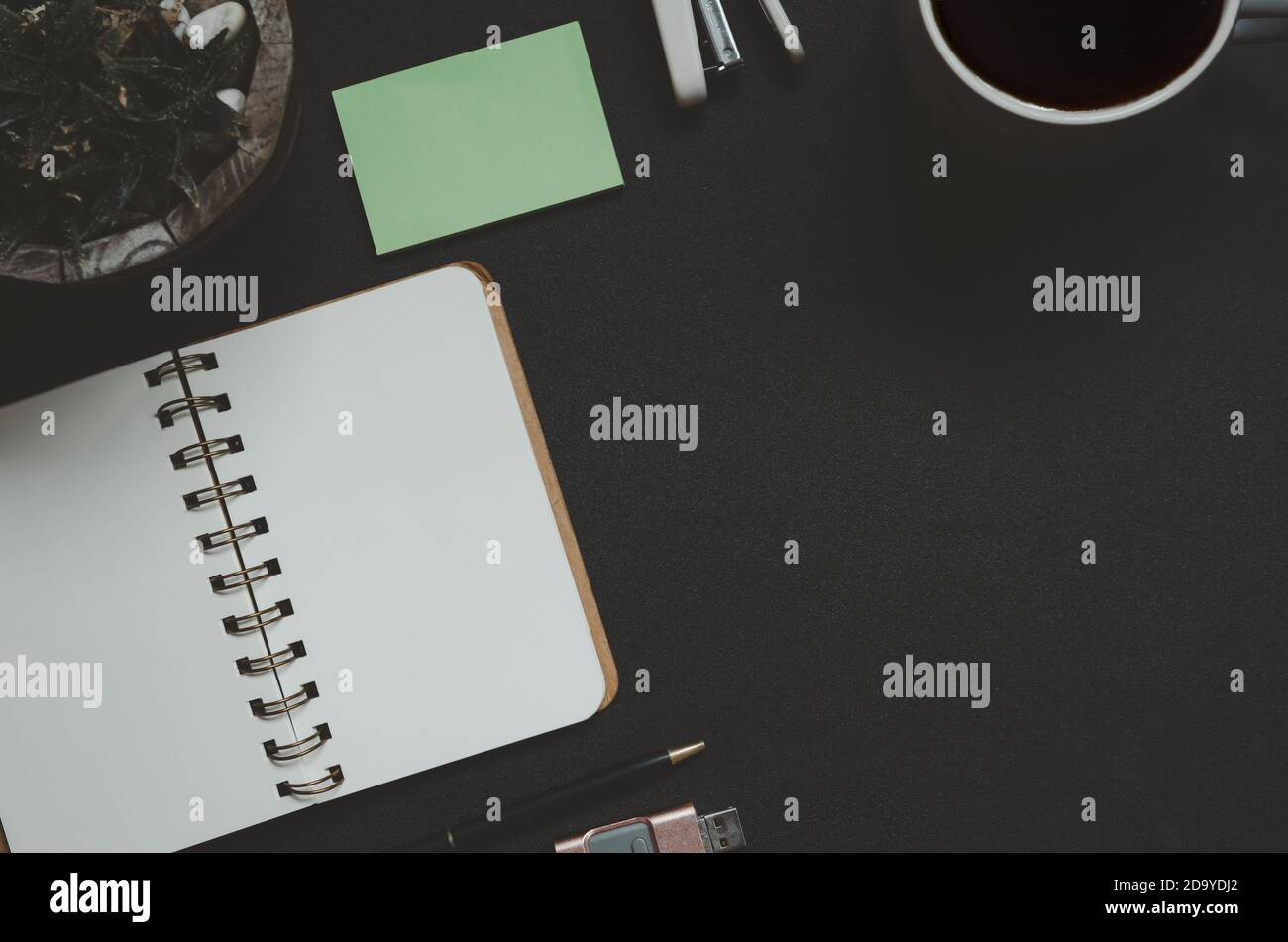Schreibtisch mit Notizblock, Kaffee, Blatt und Stift auf schwarzem Hintergrund.Draufsicht copy space.Vintage Ton Stockfoto