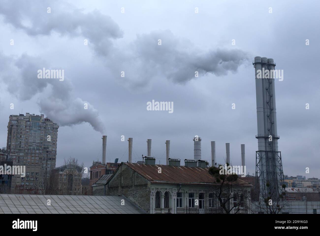 Rauch kommt von Industrieschornsteinen über den Dächern. Der Himmel ist mit grauen Wolken bedeckt. Umweltverschmutzung. Stockfoto