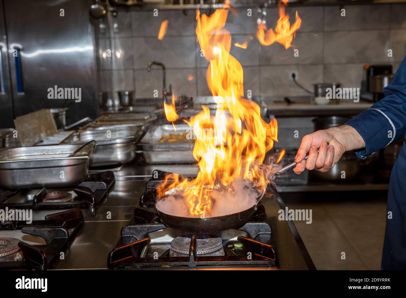 Flamme in der Pfanne. Der professionelle Koch stellt in der Restaurantküche Flambe für das Essen zu. Koch kocht mit offenem Kamin auf einem Herd. Stockfoto