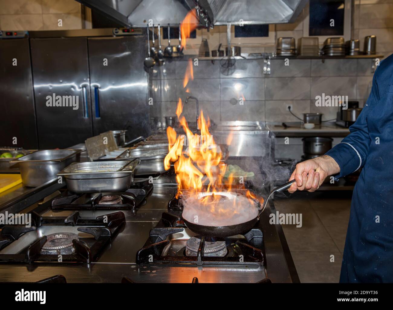 Flamme in der Pfanne. Der professionelle Koch stellt in der Restaurantküche Flambe für das Essen zu. Koch kocht mit offenem Kamin auf einem Herd. Stockfoto