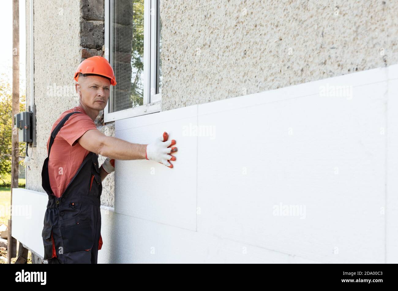 Isolierung des Hauses mit Polyfoam. Der Arbeiter installiert eine Styroporplatte an der Fassade. Stockfoto