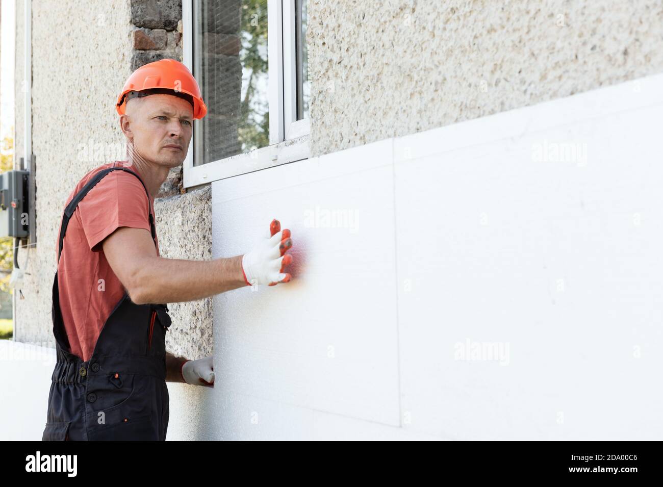 Isolierung des Hauses mit Polyfoam. Der Arbeiter installiert eine Styroporplatte an der Fassade. Stockfoto