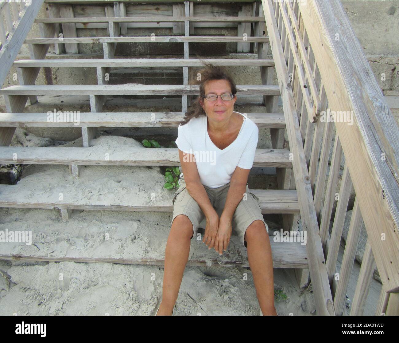 Eine Frau, die auf einer Treppe von einer Promenade zu sitzt Ein Sandstrand an einem Sommertag Stockfoto