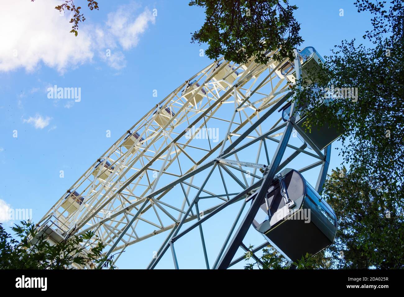 Riesenrad durch grünen Baum auf dem Hintergrund des blauen Himmels in sonnigen Sommertag, Ansicht von unten. Stockfoto