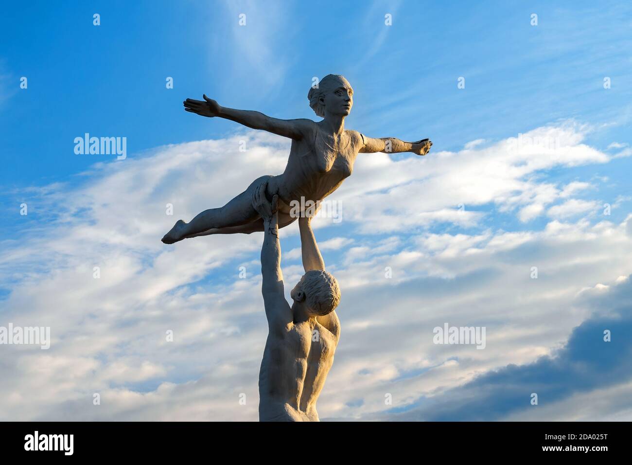 Sowjetische Parkskulptur aus Fiberglas, Mann hält Frau über den Kopf gegen blauen Himmel mit Wolken. Stockfoto
