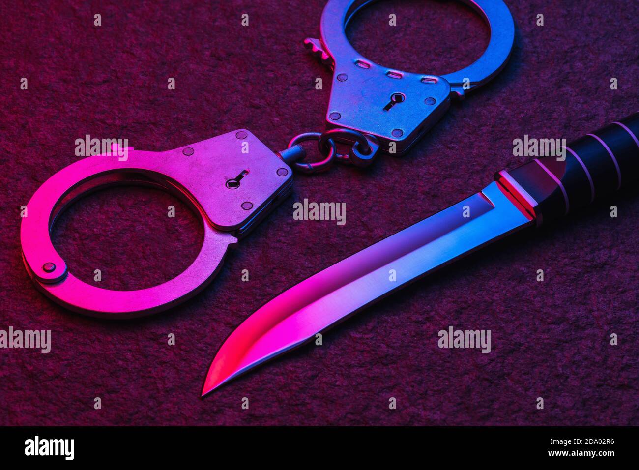 Handschellen und ein Messer auf einer Steinoberfläche mit mehrfarbigem Licht beleuchtet. Konzept zum Thema Bestrafung für ein begangenen Verbrechen Stockfoto