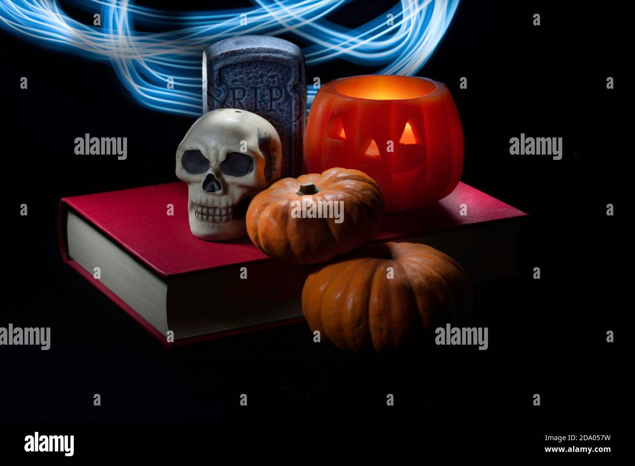 Halloween-Dekorationen und Miniatur-Kürbisse auf einem roten Buch isoliert In schwarzem Hintergrund und beleuchtet mit beweglichen blauen LED-Taschenlampe Stockfoto