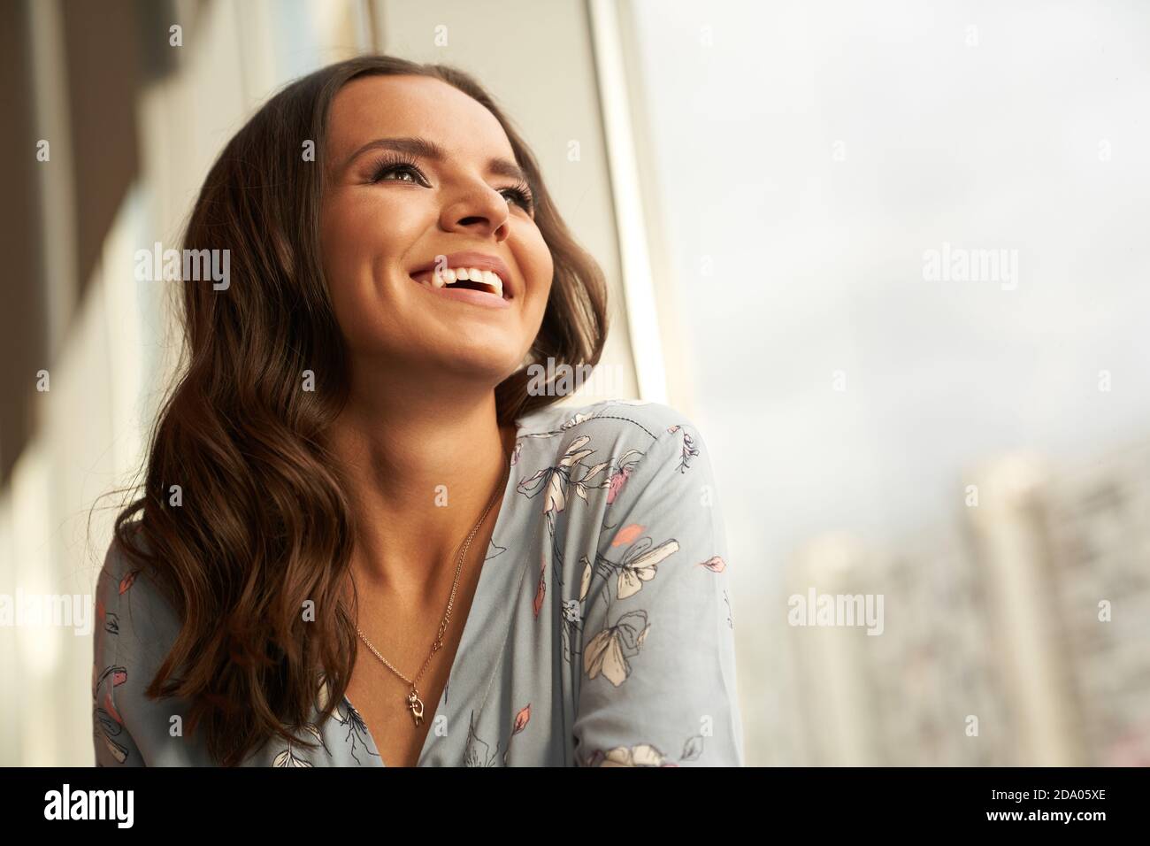 Eine schöne junge Frau glücklich und lächelnd blickt zum Fenster, das Mädchen hat perfekte Haut und ein schneeweißes Lächeln Stockfoto
