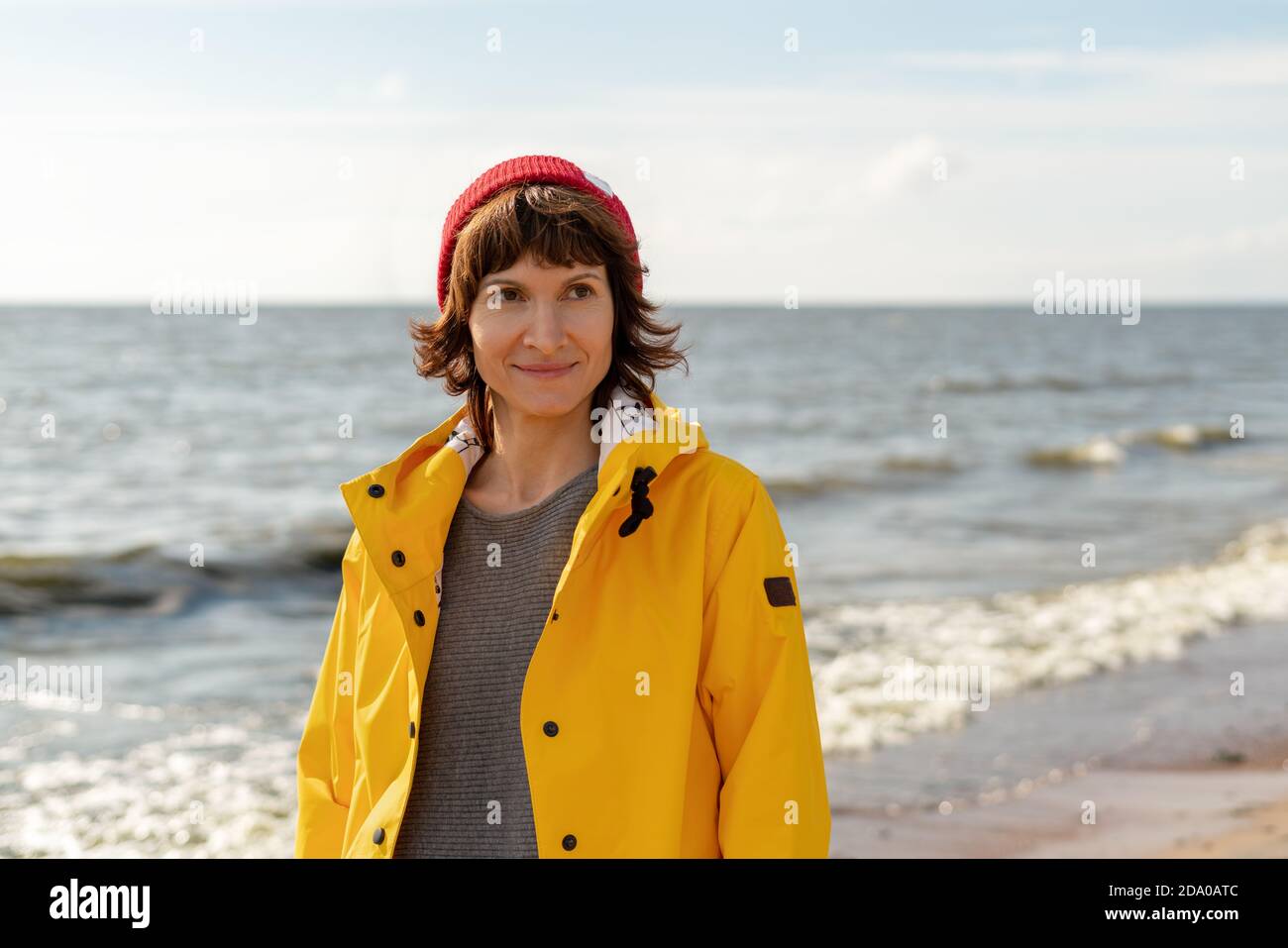 Taille Porträt der reifen Frau in hellen gelben Umhang und Red hat am Ufer Stockfoto