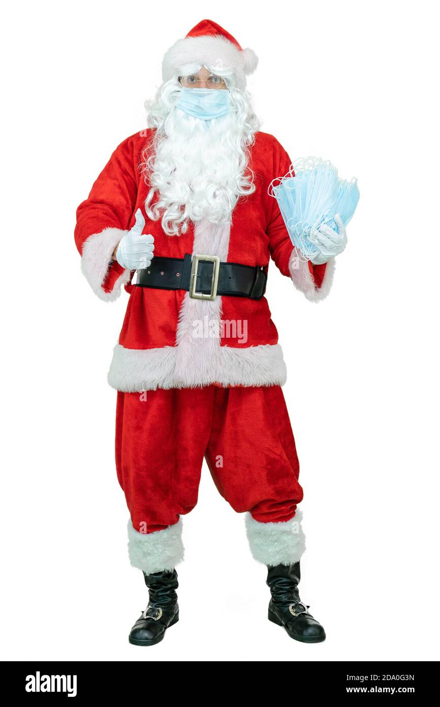 Santa Claus trägt eine covid medizinische Maske, hält Maske oder Atemschutzmasken Epidemie oder Coronavirus Schutz. Der Weihnachtsmann zeigt den Daumen nach oben Stockfoto