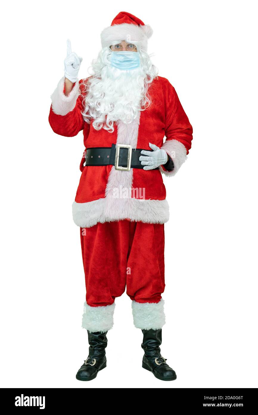 Santa tragen in einer covid medizinische Maske, zeigt Zeigefinger nach oben. Ganzkörper-Weihnachtsmann zeigt Zeigefinger iup auf weißem Hintergrund. Weihnachten steht bevor Stockfoto