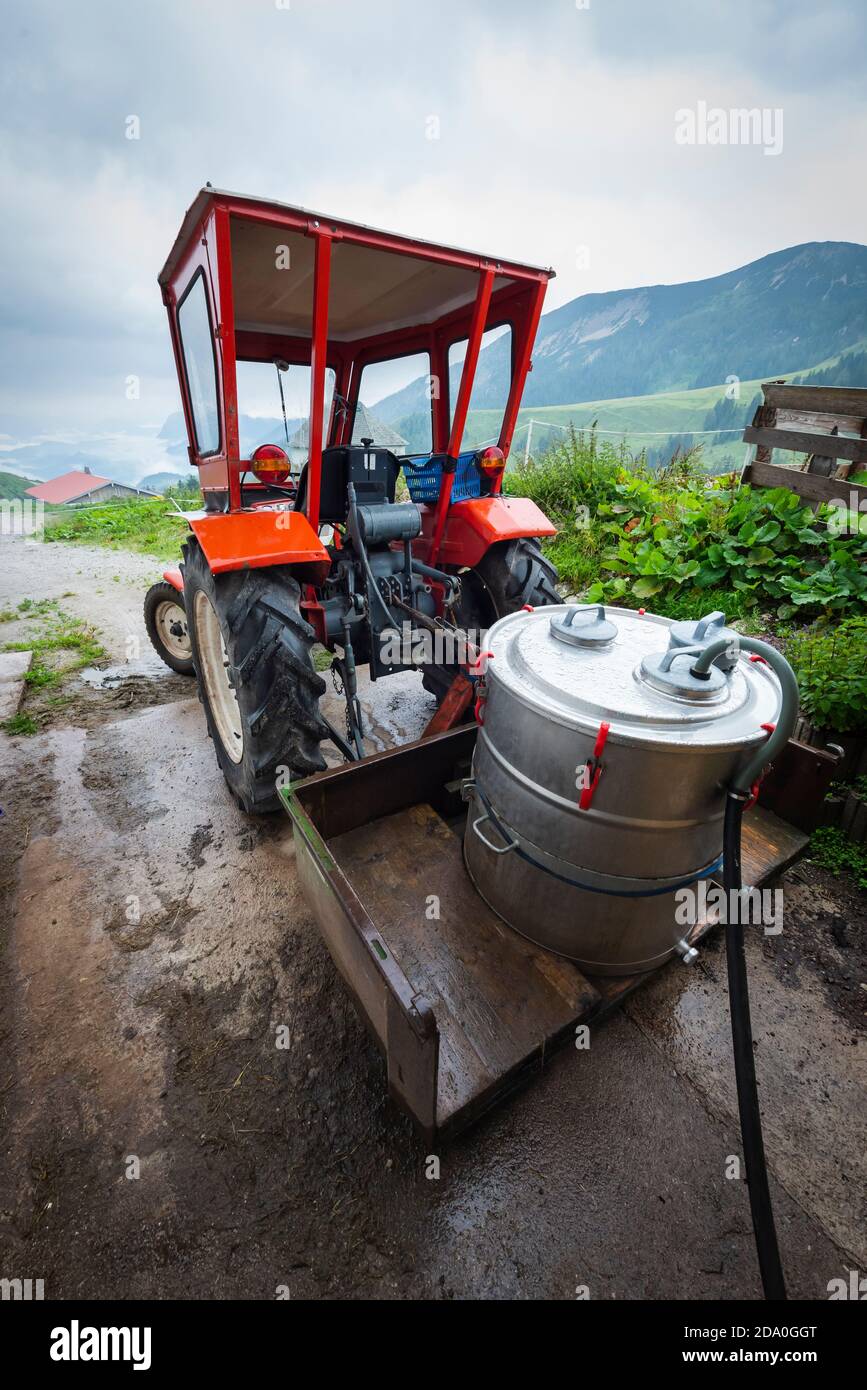 Ein Edelstahlmilchfass wird mit Milch gefüllt auf dem Anhänger eines roten Linder Traktors auf der Ackernalm, Tirol, Österreich Stockfoto