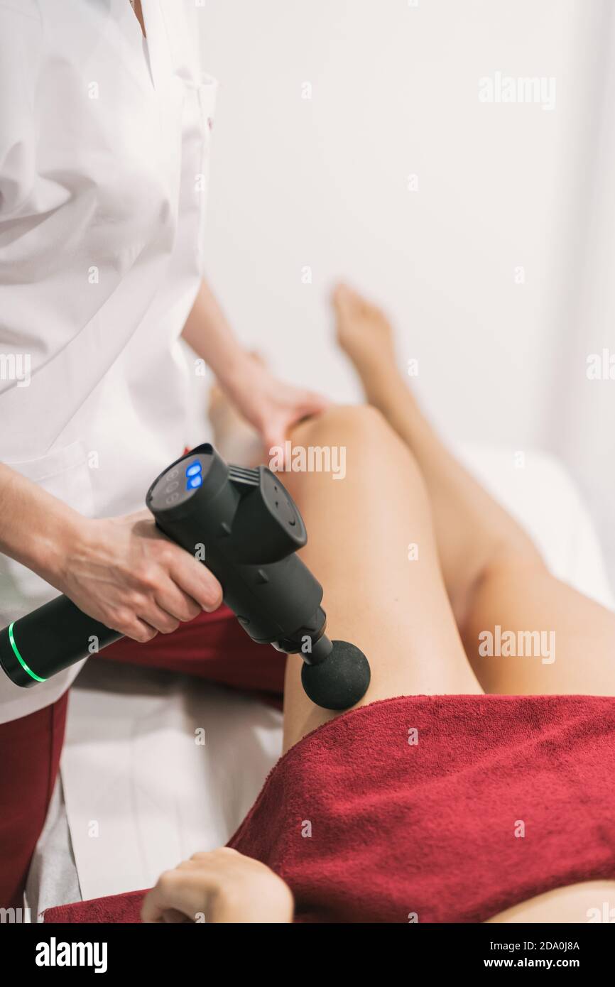 Weibliche Physiotherapeutin mit Massagepistole auf Bein des Patienten  während Perkussive Therapie im modernen Krankenhaus Stockfotografie - Alamy