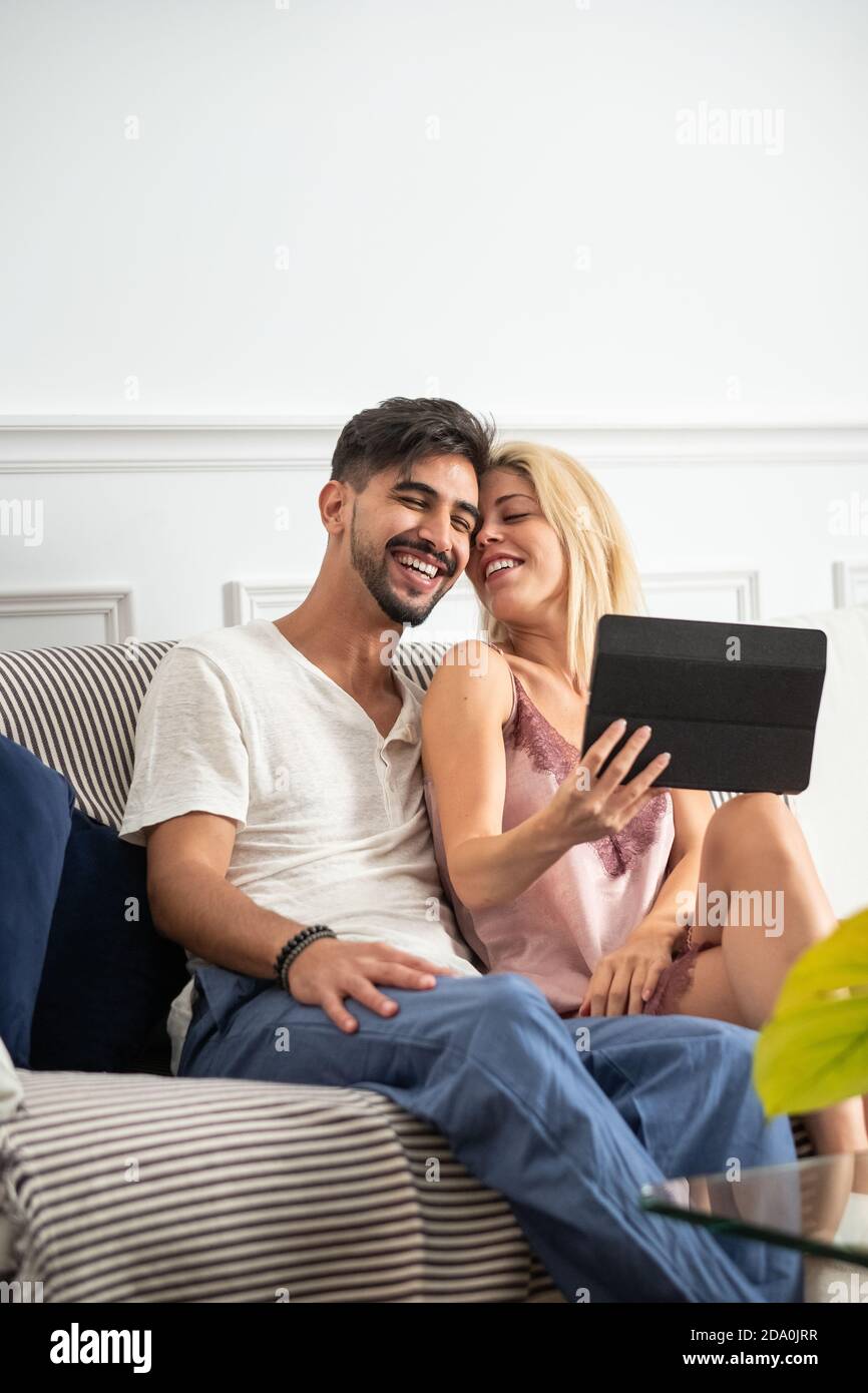 Glückliches junges Paar Kuscheln und Browsen Tablet beim Sitzen zusammen auf dem