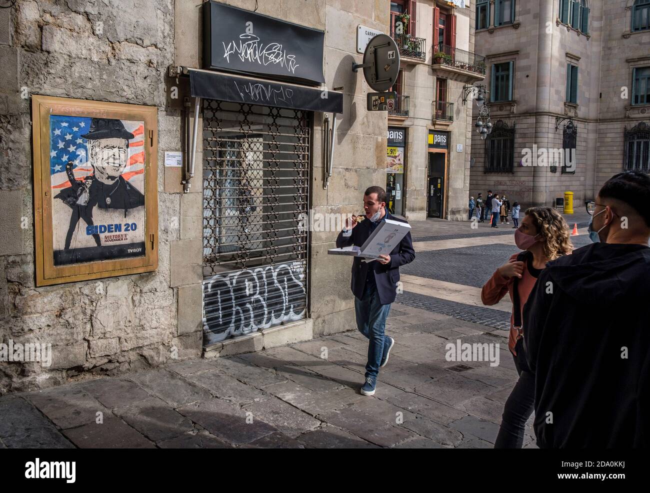 Barcelona, Katalonien, Spanien. November 2020. Ein Mann, der Pizza isst, läuft an den neuen Graffiti vorbei.Street Graffiti-Künstler tvBoy hat ein neues Stück auf der Plaza Sant Jaume gemacht, um Joe Bidens Sieg bei den US-Wahlen zu feiern. Kredit: Paco Freire/SOPA Images/ZUMA Wire/Alamy Live Nachrichten Stockfoto