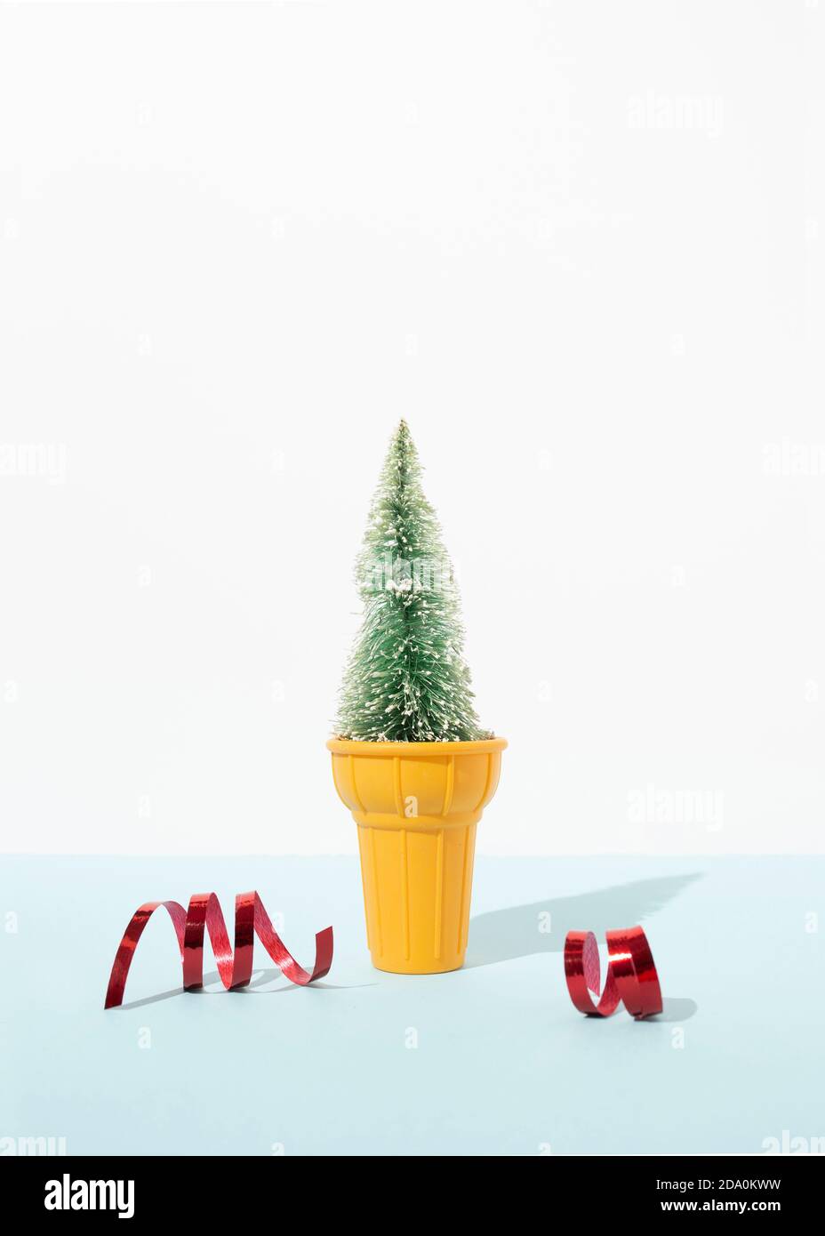 Miniatur-Weihnachtsbaum in dekorativen Eisbecher platziert auf Tisch mit roten glänzenden Bändern im Studio auf blauem Hintergrund Stockfoto