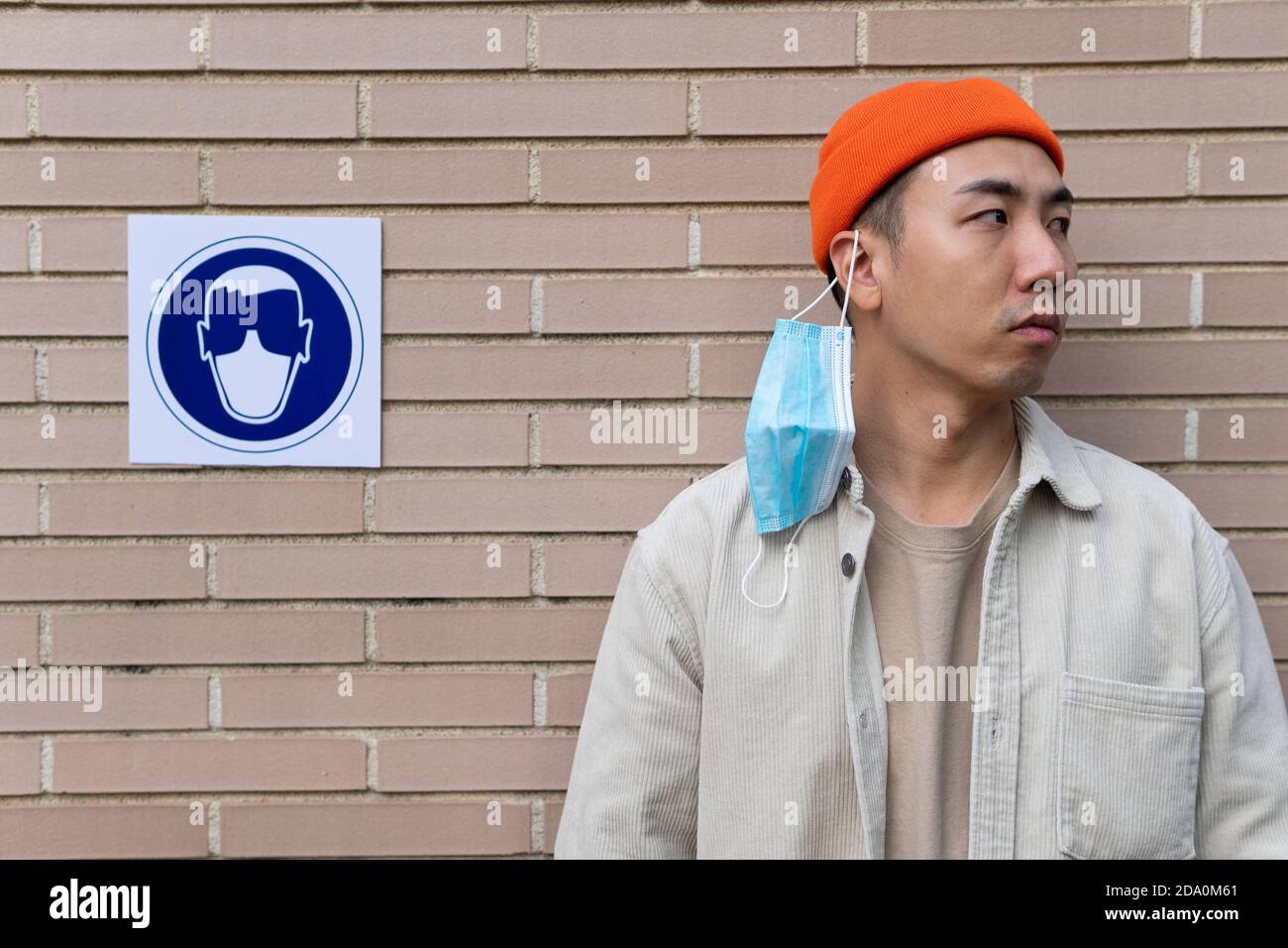 Ernsthafte asiatische männliche Bremsregel, indem sie aus Maske stehen In der Nähe Schild in Gebäudewand illustrieren Person in Schutzmaske Stockfoto
