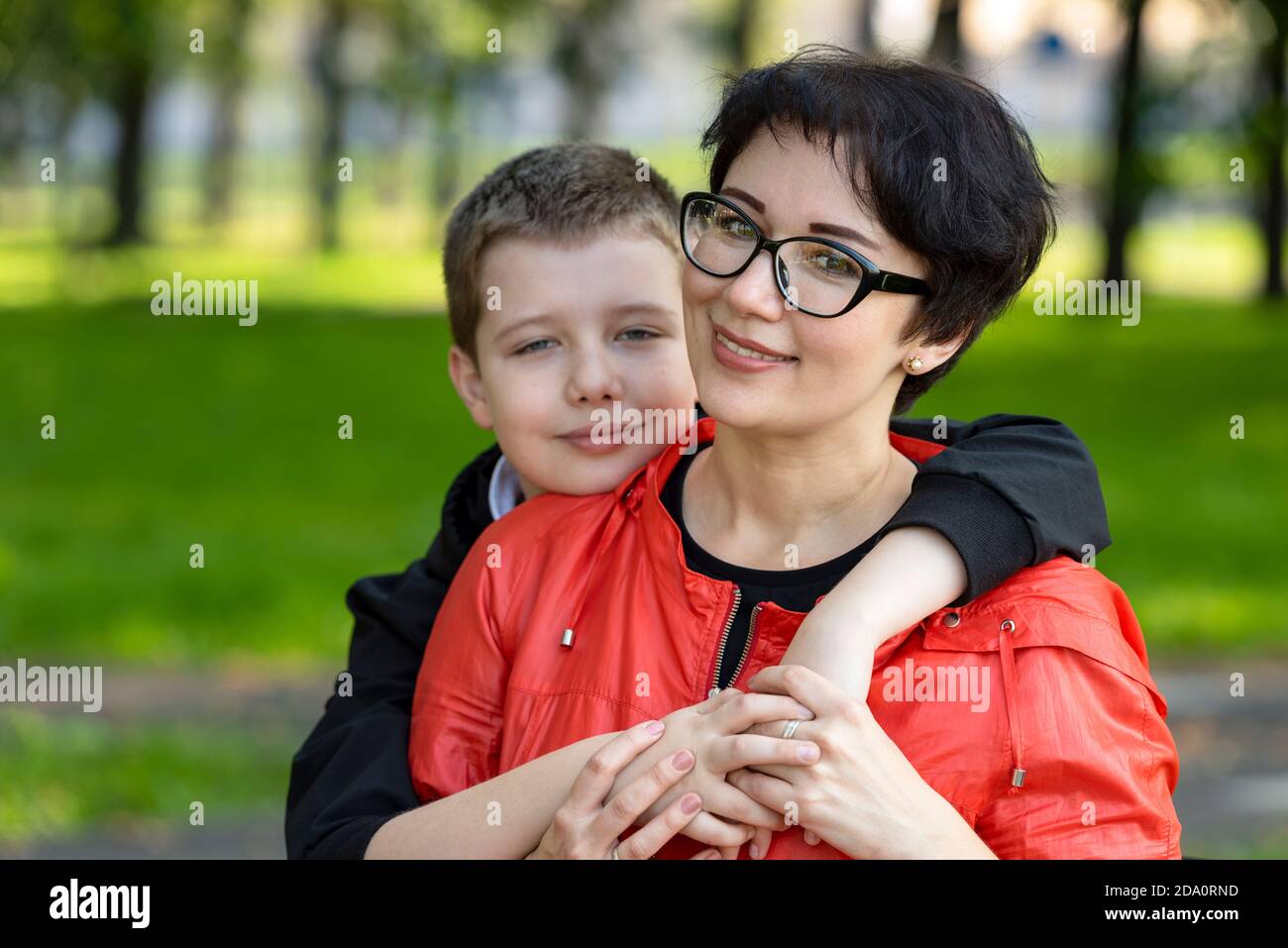 Porträt einer glücklichen Mutter, Teenager Sohn umarmt sie. Familienfreizeit in der Natur im Park, sonniger Herbsttag. Gesunde Beziehungen, Nähe. Stockfoto