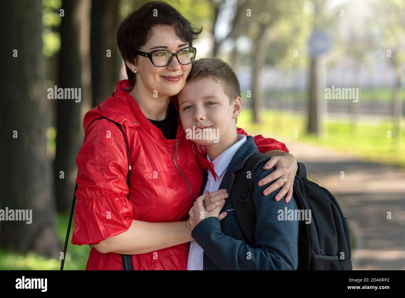 Glückliche Mutter und Sohn umarmen einander. Mutter und teen Sohn im die Park nach der Schule. Die Liebe einer Mutter, die Erziehung von Kindern, vertrauensvolle Familienbeziehungen Stockfoto