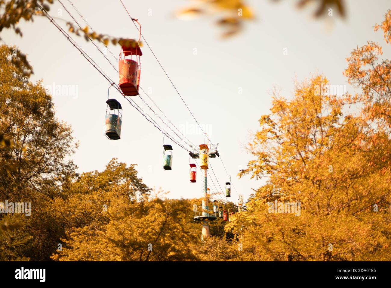 Seilbahn mit bunten Taxis über grünen Wäldern mit blau bewölktem Himmel auf dem Hintergrund. Herbstzeit Stockfoto