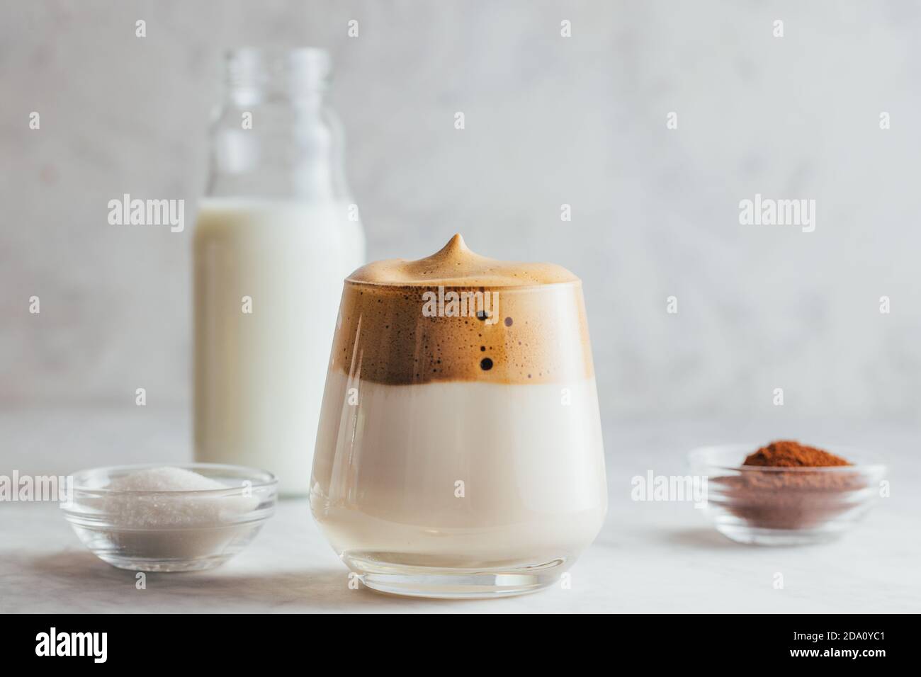 Aromatisches Dalgona-Getränk aus Glas auf Marmortisch mit einer Flasche Milch, Instant-Kaffee und Bohnen Stockfoto