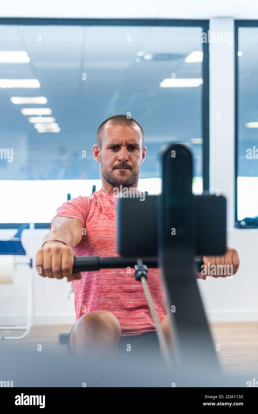 Konzentrierter athletischer Mann, der beim Training Übungen am Rudergerät macht Im modernen Fitnessraum Stockfoto