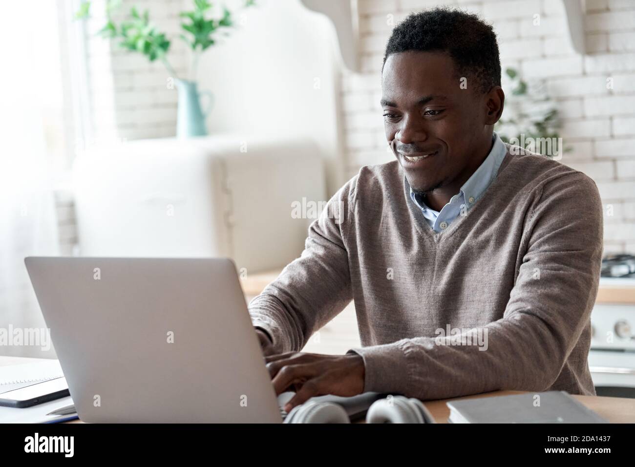 Lächelnder afroamerikanischer Mann mit Laptop-Computer, der vom Heimbüro aus arbeitet. Stockfoto
