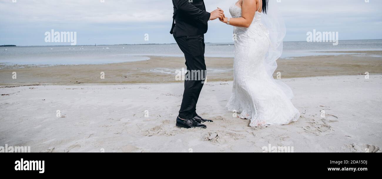 Brautpaar tanzt am Strand, junge Braut trägt weißes Kleid und langen Schleier. Stockfoto