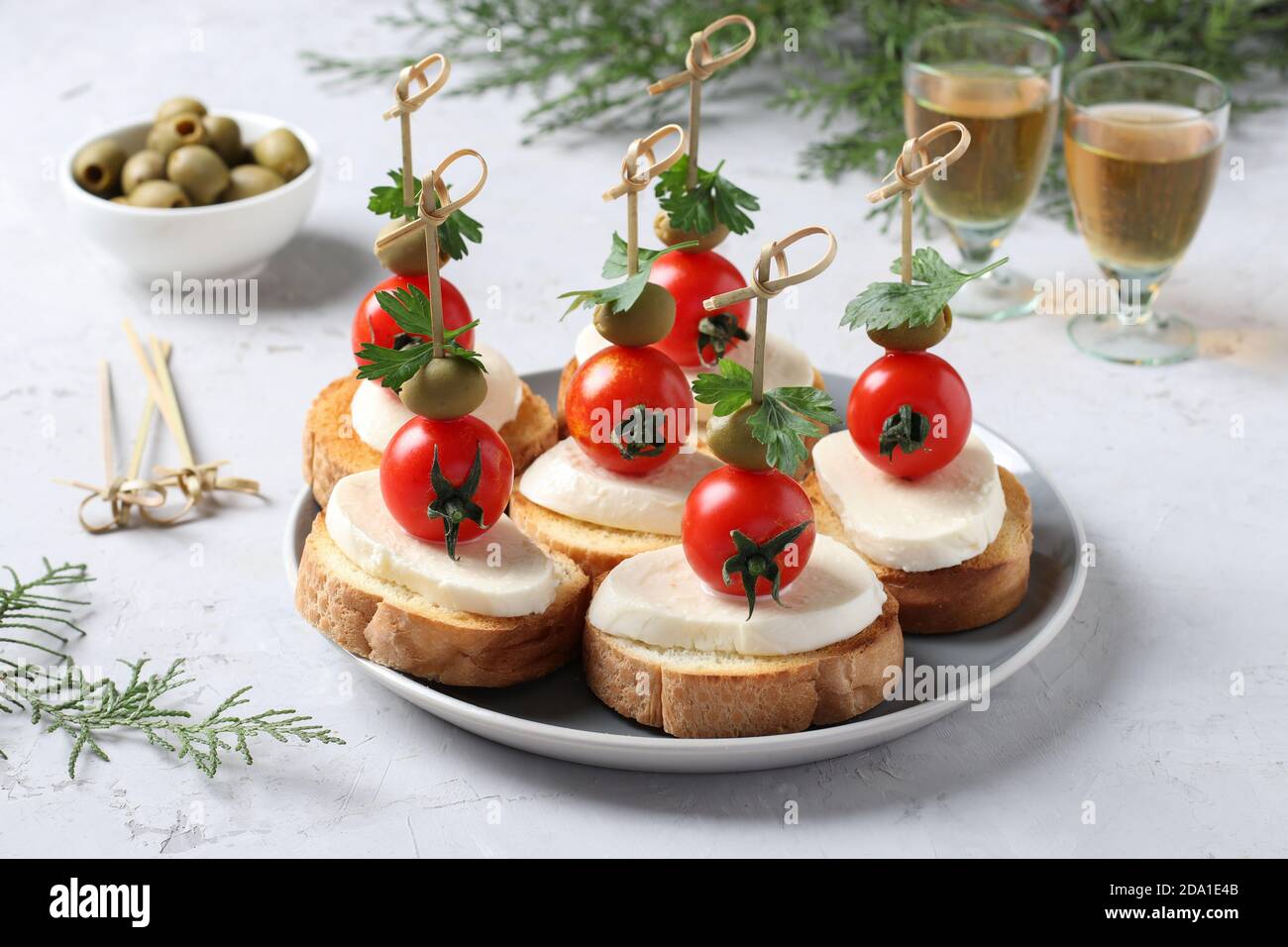 Kanapees von Mozzarella, Kirschtomaten, grüne Oliven, Petersilie auf Croutons von weißem Brot auf grauem Hintergrund. Festlicher Neujahrsnack. Nahaufnahme Stockfoto