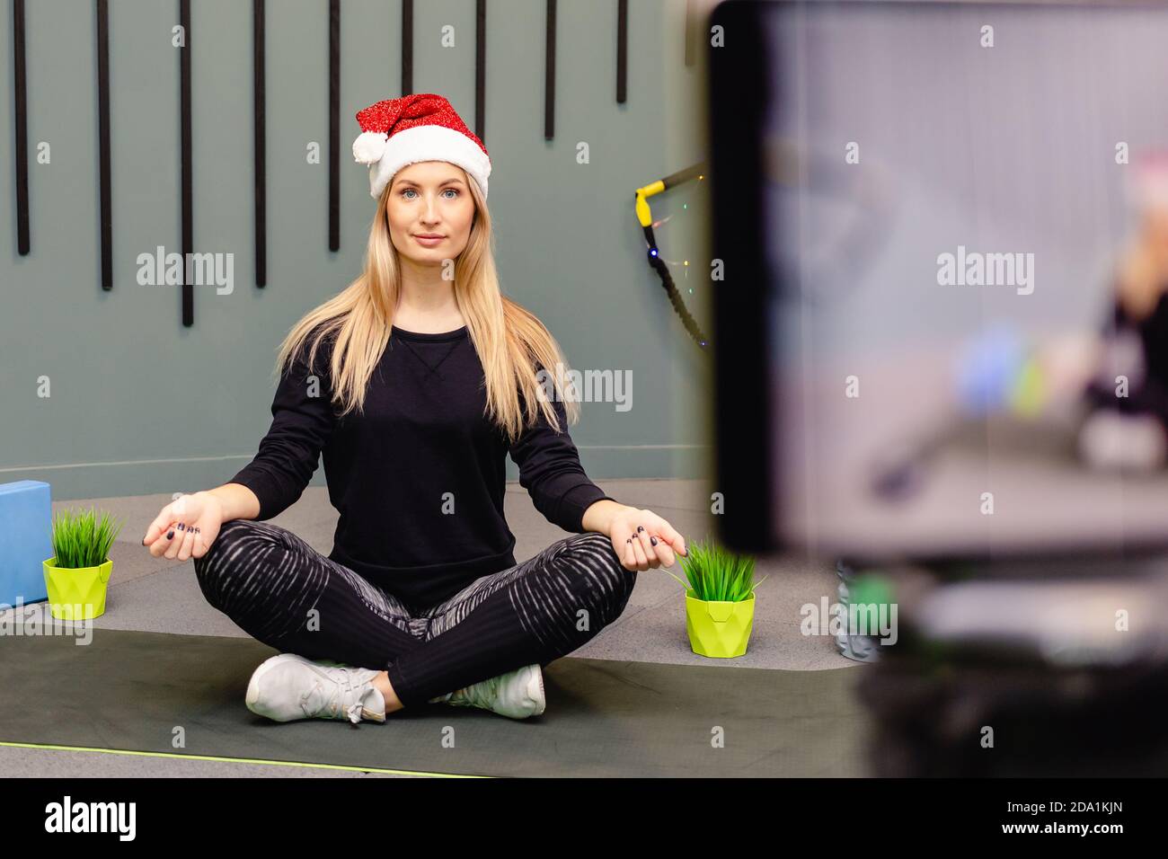 Ein Mädchen in einem Weihnachtsmütze, ein Sportoutfit zeichnet Trainingsvideos auf KameraNotieren Sie eine Videostunde über Trainingssport für den Kanal im Internet. Blog Stockfoto