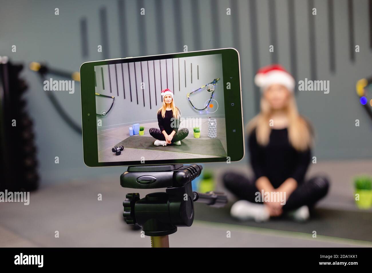 Frau in Santa hat Fitness-Trainer Aufnahme Video-Blog mit Kamera auf Stativ. Live-Streaming, Social Media, Netzwerk, Blogging, Trainingskonzept. Stockfoto