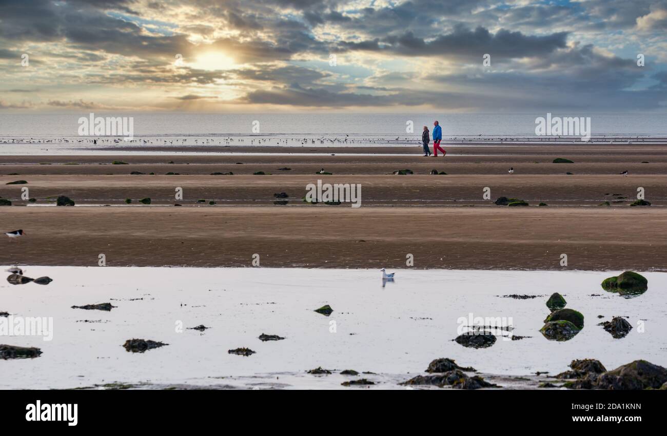 Paar, die bei Ebbe am Sandstrand spazieren gehen, mit farbenprächtiger Abenddämmerung am Himmel bei Sonnenuntergang, Firth of Forth, Schottland, Großbritannien Stockfoto