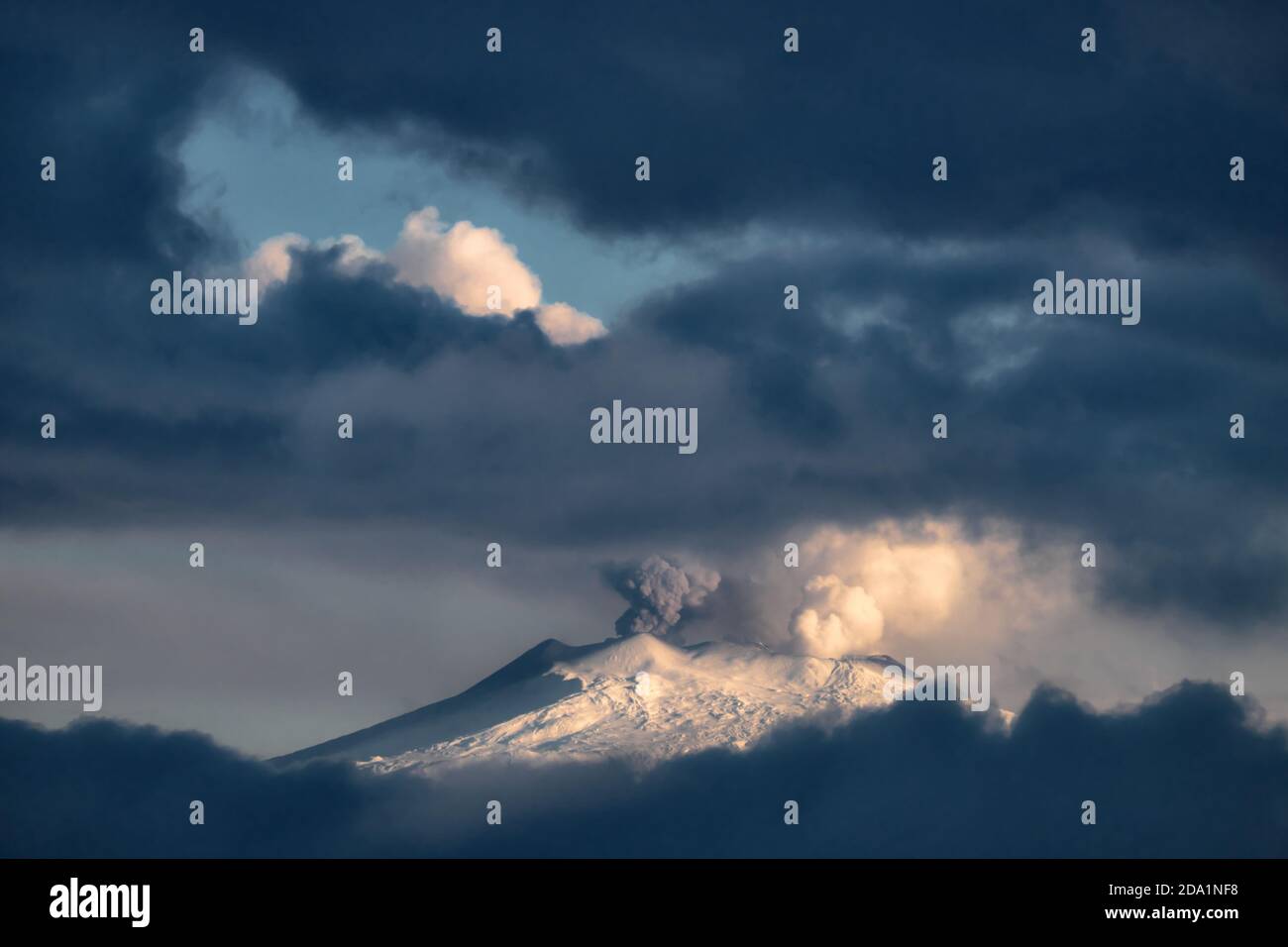 Der schneebedeckte Ätna Mountain strahlt Rauch aus dem zentralen Krater aus, der von stürmischen niedrigen Wolken eingerahmt wird; der Vulkan ist ein natürliches Wahrzeichen Siziliens Stockfoto