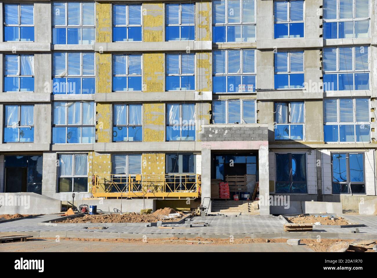 Bau eines neuen mehrstöckigen Gebäudes. Aufgehängte Wiege für Arbeiten Dämmung der Fassade der Mineralwolle. Verlegung von Pflasterplatten. Moderne Resi Stockfoto