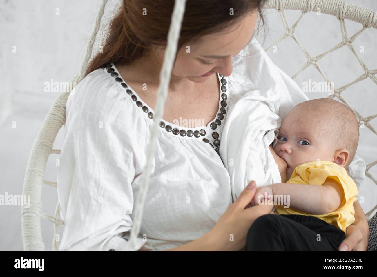 Glückliche Mutter füttert das Baby in einer weißen Hängematte auf einem weißen Hintergrund Nahaufnahme. Happy Mutterschaft Konzept. Stockfoto