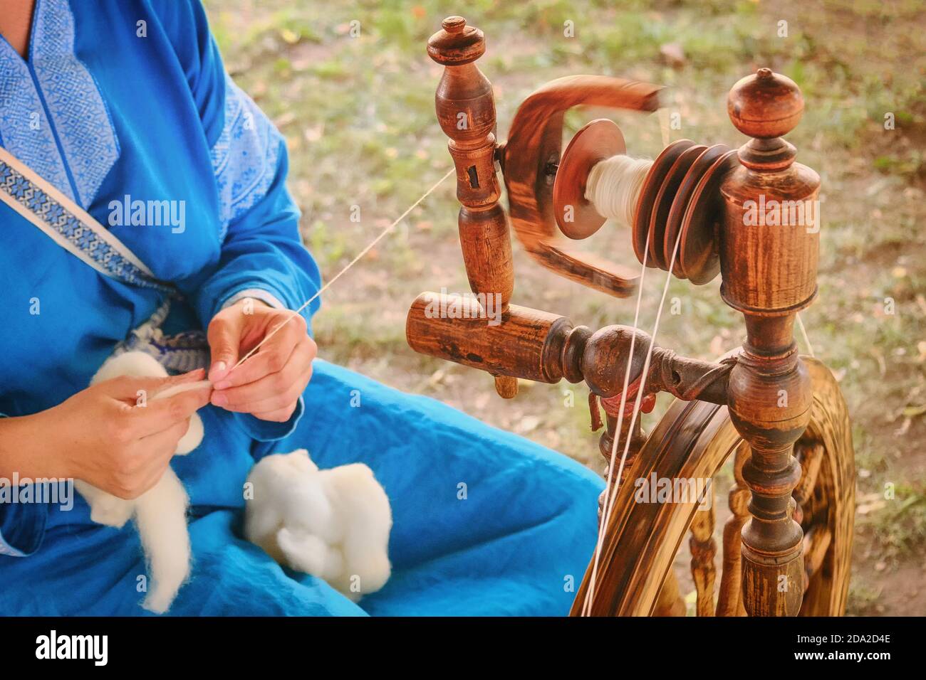 Ditstaff erzeugt ein Gewinde aus einer Spindel. Manuelles Spinnrad im Freien, Lifestyle. Stockfoto